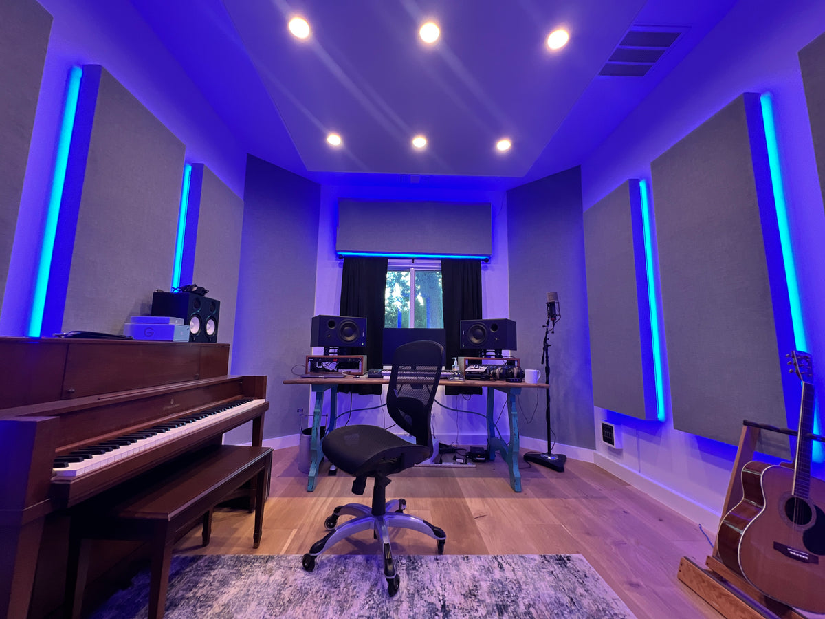 Home studio with blue backlit acoustic wall panels, a desk between studio monitors and an upright piano