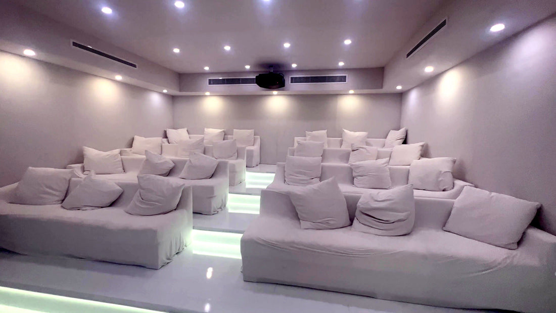 All-white listening room with tiered risers lit from below, white sofas and a ceiling projector