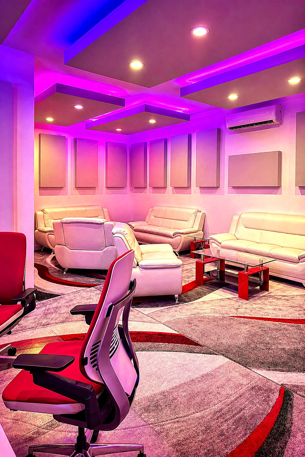Client lounge with acoustic ceiling clouds edge-lit in pink and violet LED, a row of fabric wall panels and white leather seating
