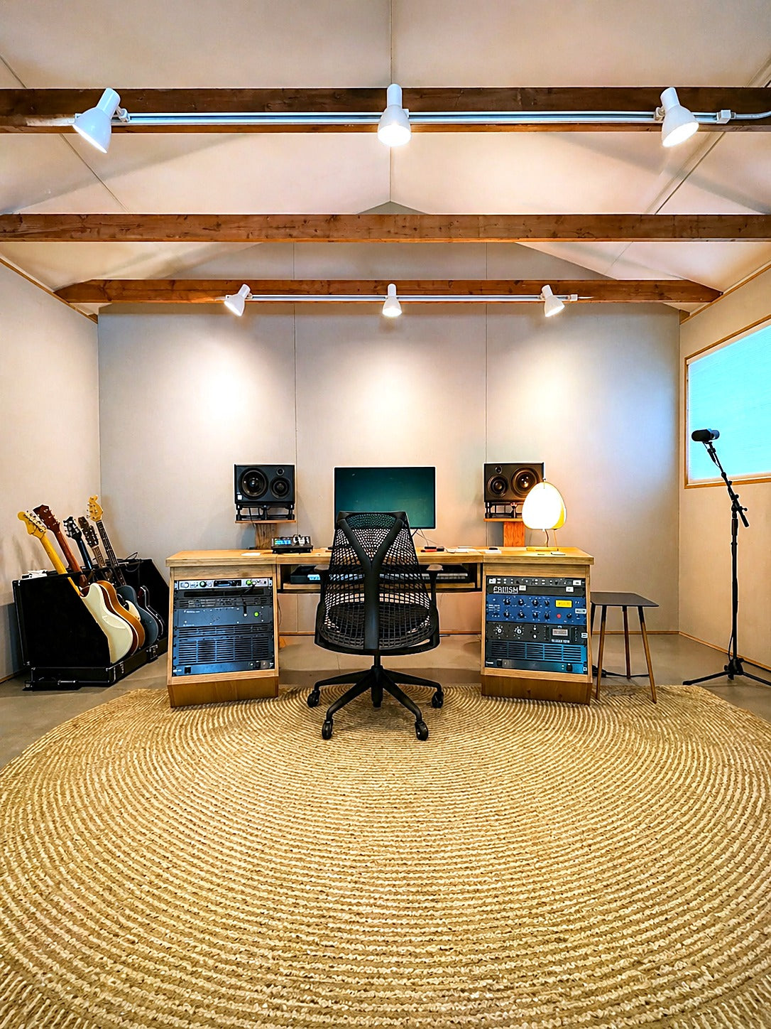 Mix room with fabric-wrapped walls under exposed wood ceiling beams, a custom wood desk with rack bays and a round jute rug
