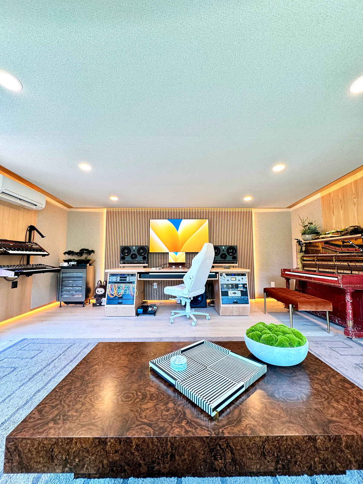 Production room with slat wood walls, a custom desk, keyboards and an upright piano