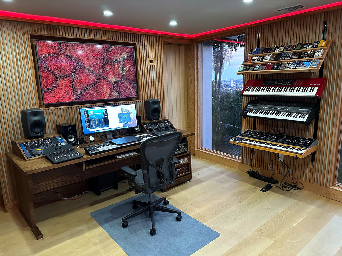 Production room with slat wood walls, red LED cove lighting, a wood desk and a tiered synthesizer rack