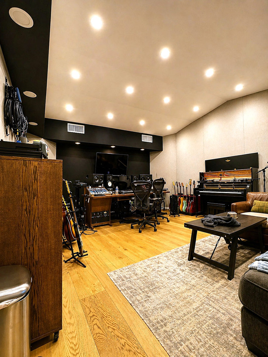 Control room with fabric-wrapped walls, a black front soffit with recessed lighting, a row of guitars and an upright piano
