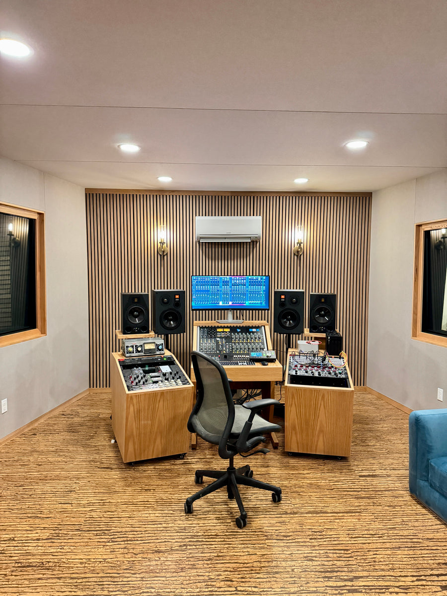 Control room with a slatted wood front wall, fabric acoustic panels on the side walls and wood console furniture