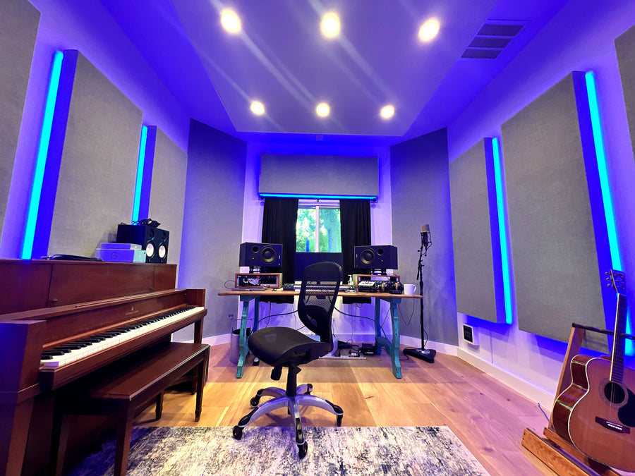 Home studio with blue backlit wall panels, a desk between the monitors and an upright piano