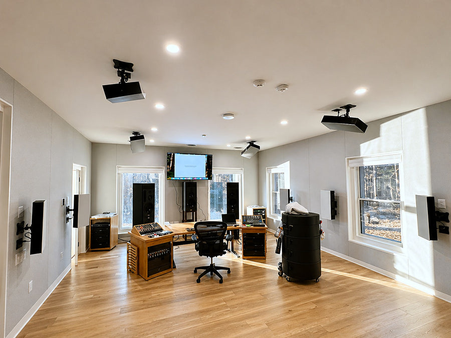 Immersive surround control room with fabric-wrapped acoustic wall panels, ceiling-mounted speakers and a wood console desk