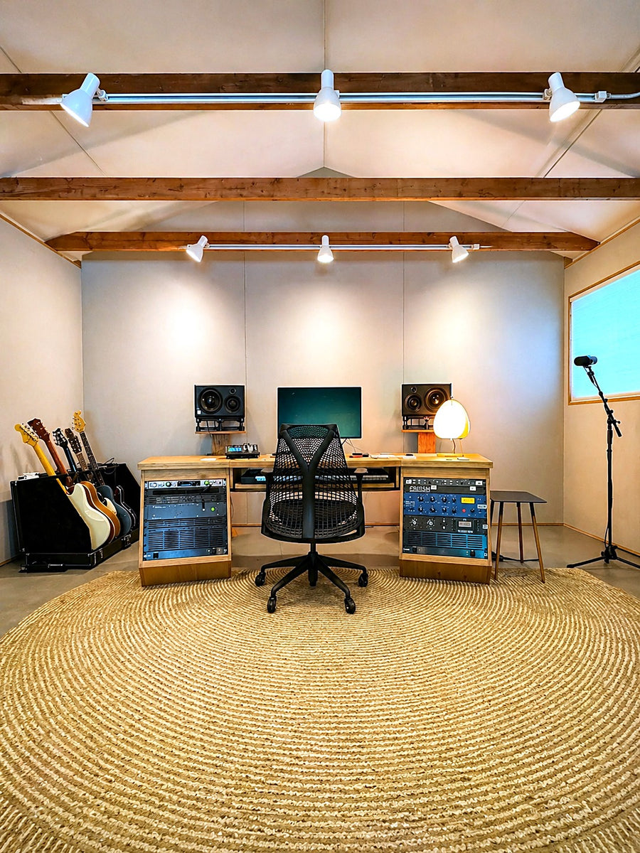Mix room with fabric-wrapped walls under exposed wood ceiling beams, a custom wood desk with rack bays and a round jute rug